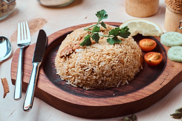 Plato tradicional indio con arroz, limón, tomate, hojas de cilantro y cubiertos en bandeja de madera.
