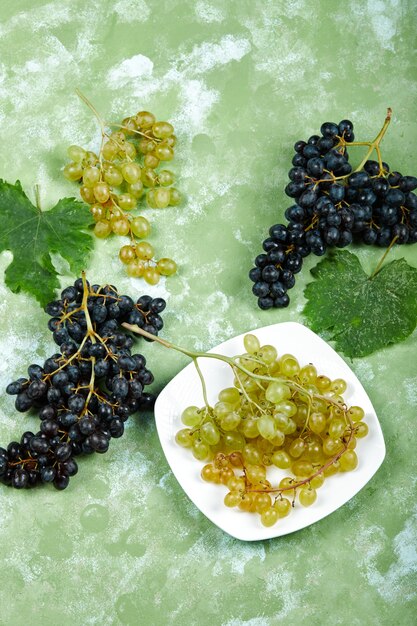 Foto gratuita un plato de uvas blancas y uvas negras con hojas sobre superficie verde