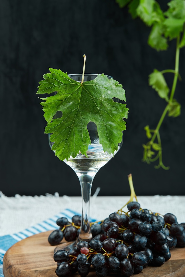 Foto gratuito un plato de uvas negras y una copa de vino con hojas sobre fondo oscuro. foto de alta calidad