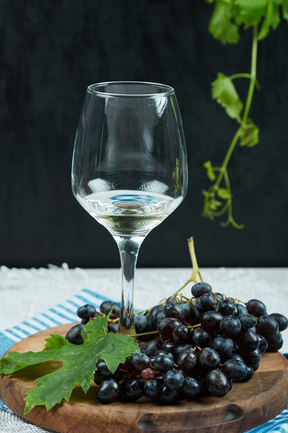 Un plato de uvas negras con hojas y una copa de vino sobre una superficie oscura