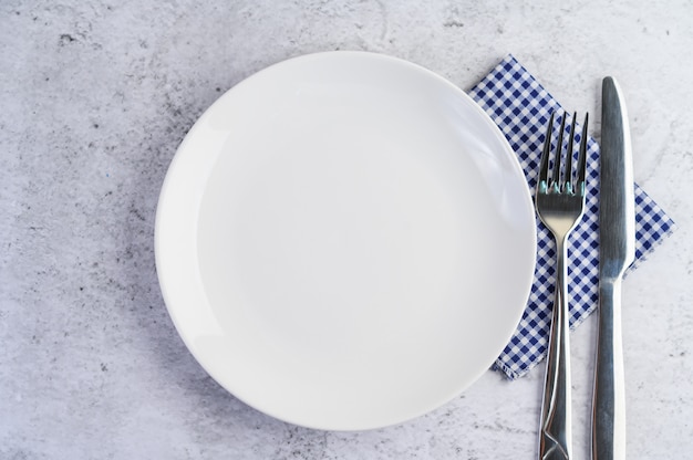 Foto gratuita plato vacío blanco con tenedor y un cuchillo sobre un mantel azul-blanco.