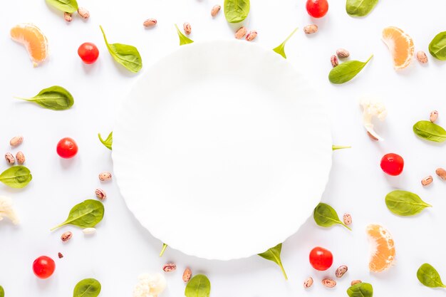 Plato vacío rodeado de frijol pinto; Verduras y rodajas de naranja dispuestas sobre fondo blanco