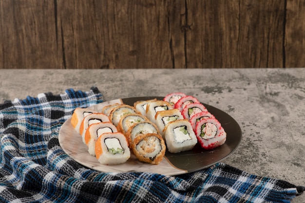 Plato de varios deliciosos rollos de sushi sobre mesa de mármol