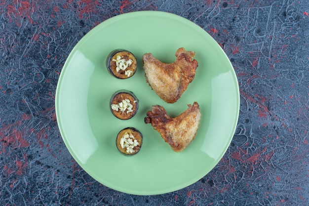 Un plato verde de carne de pollo y rodajas de berenjena frita.