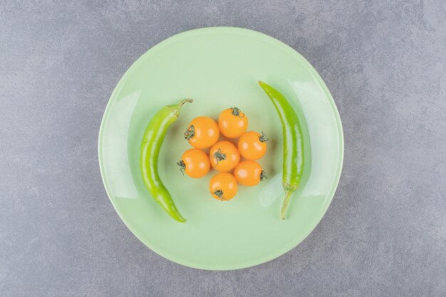 Un plato verde con tomates cherry amarillos y chiles