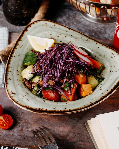 Un plato de verduras asadas con rodajas de col roja y limón.