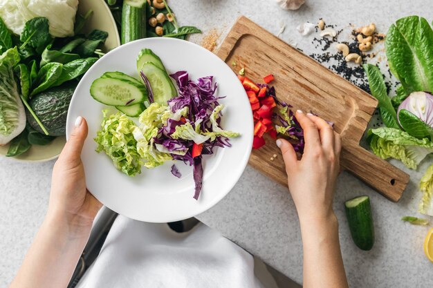 Un plato con verduras frescas picadas en manos femeninas en la vista superior de la cocina