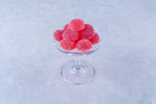 Un plato de vidrio lleno de caramelos de gelatina de frutas azucaradas rojas sobre una mesa gris.