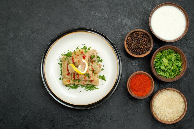 Plato de vista superior y especias repollo relleno con salsa de limón y hierbas y cuencos de especias coloridas hierbas arroz crema agria y pimienta negra sobre mesa de madera