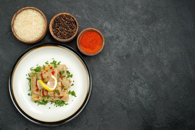 Plato de vista superior y especias repollo relleno con salsa de limón y hierbas y tazones de especias coloridas, arroz y pimienta negra en el lado izquierdo de la mesa de madera