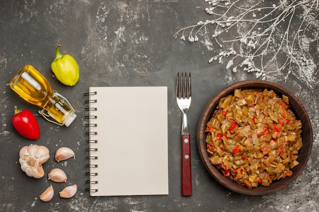 Foto gratuita plato de vista superior de frijoles ajo pimientos aceite en botella junto al tenedor cuaderno blanco y plato de judías verdes y tomates en la mesa