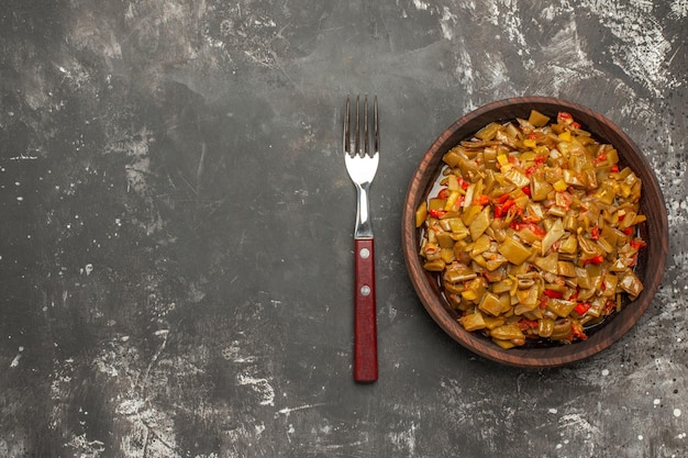 Plato de vista superior de primer plano de judías verdes Plato marrón de apetitosas judías verdes y tomates junto al tenedor en el lado derecho de la mesa oscura