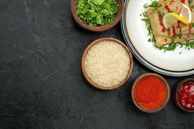 Plato de vista superior de primer plano con salsa plato blanco de repollo relleno con hierbas de limón y salsa y especias hierbas de arroz y salsa en tazones en el lado derecho de la mesa oscura