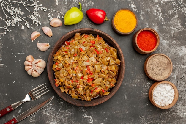 Plato de vista superior en primer plano sobre la mesa tazones de especias coloridas tomates ajo bola pimienta apetitoso plato de judías verdes junto al tenedor y cuchillo en la mesa oscura