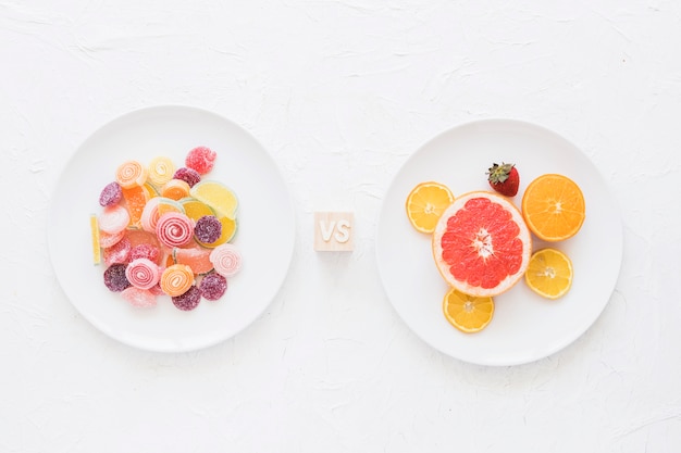 Platos de caramelos dulces frente a frutas sobre fondo blanco textura áspera