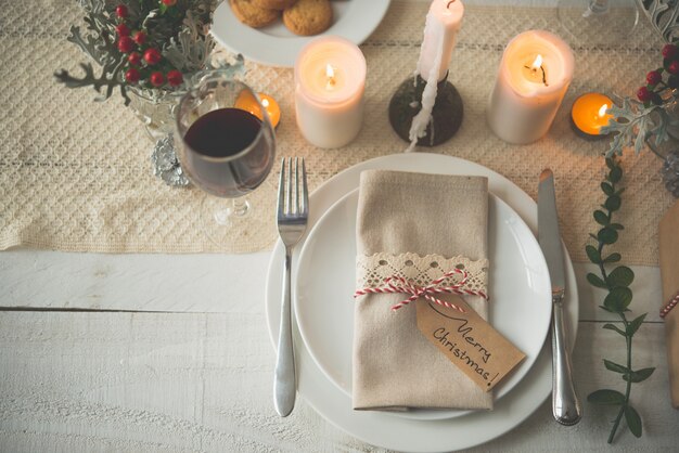 Platos, cubiertos, servilletas y copa de vino preparadas para la cena de Navidad en la mesa con velas.