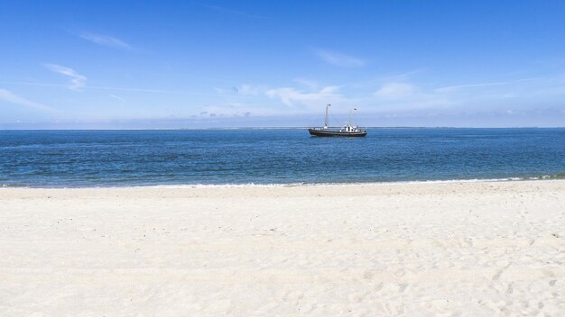 Playa de arena blanca vacía con un barco flotando en el agua