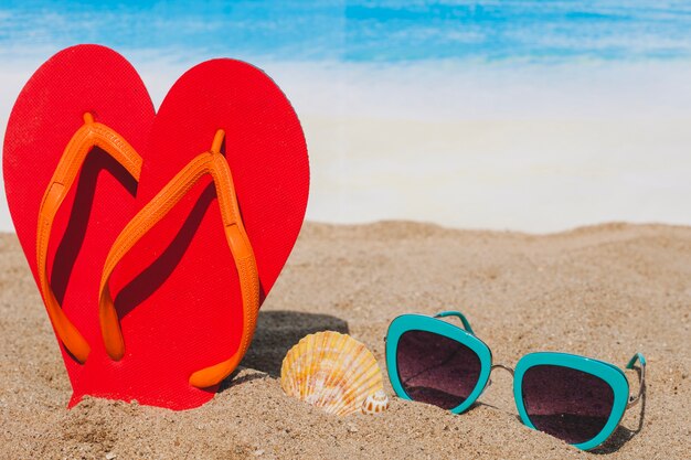 Playa con chanclas, gafas de sol y concha marina
