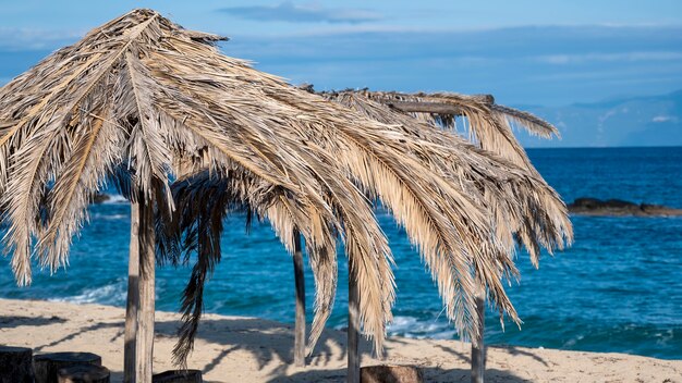 Playa del mar Egeo con sombrillas hechas de ramas de palmera en Grecia