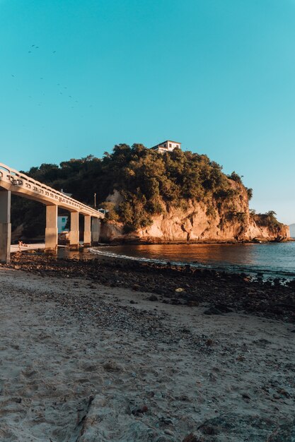 Playa rodeada por el mar y rocas cubiertas de vegetación con un puente en Brasil