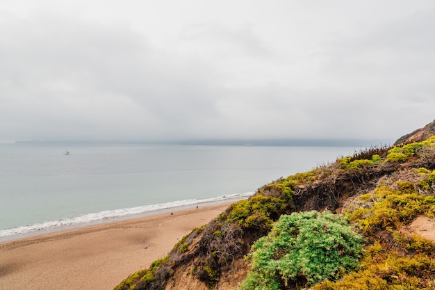 Foto gratuita playa rodeada de rocas y mar cubierto de niebla bajo un cielo nublado