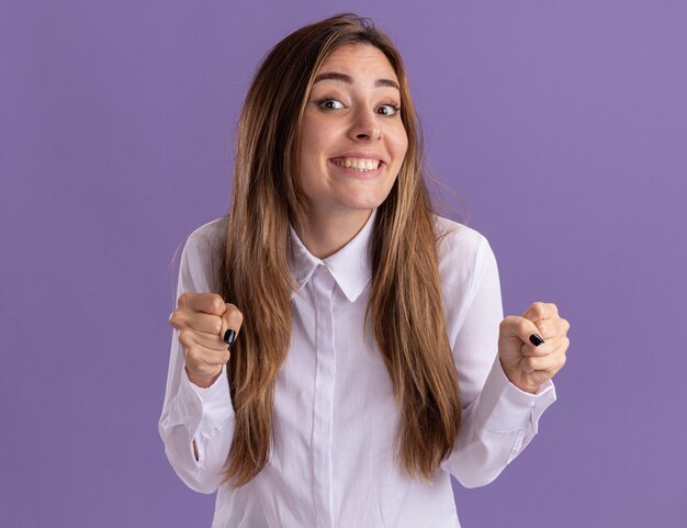 Pleased young pretty caucasian girl keeps fists on purple 