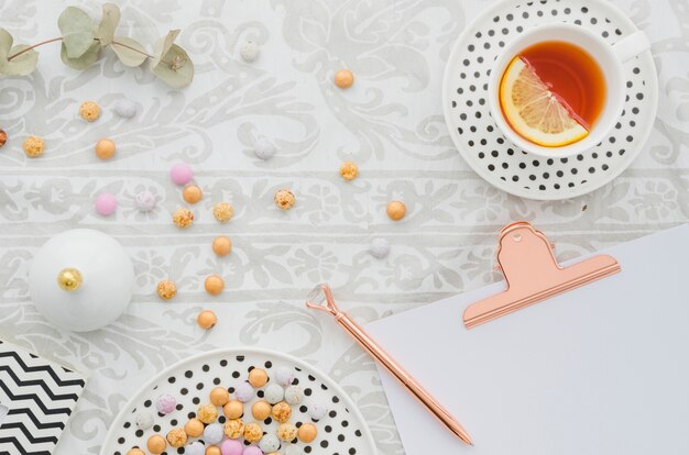 Pluma antigua en el portapapeles con caramelos y jengibre limón taza de té en el mantel