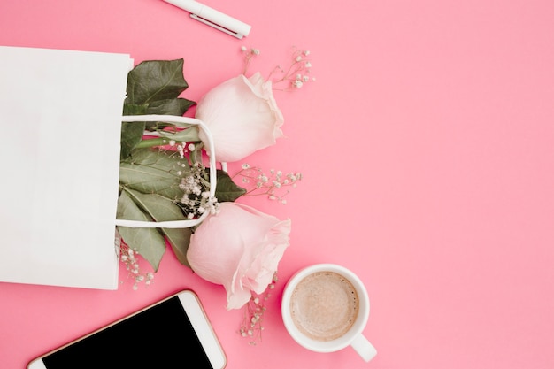 Pluma blanca rosas en la bolsa de compras; Smartphone y taza de café sobre fondo rosa