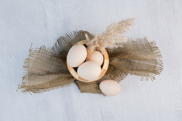 Pluma de tallos de hierba y huevos en un recipiente a cuadros sobre la mesa de mármol.