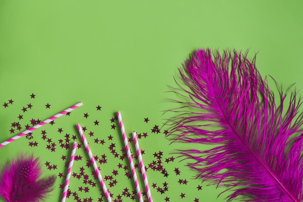 Plumas de color morado con confeti sobre una mesa verde