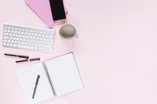 Plumas en el cuaderno espiral con el teléfono móvil y el teclado en fondo rosado