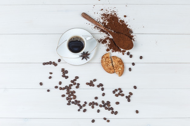 Un poco de café con café molido, especias, granos de café, galletas en una taza sobre fondo de madera, endecha plana.