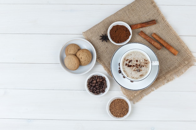 Un poco de café con granos de café, café molido, especias, galletas en una taza de madera y un pedazo de fondo de saco, vista superior.