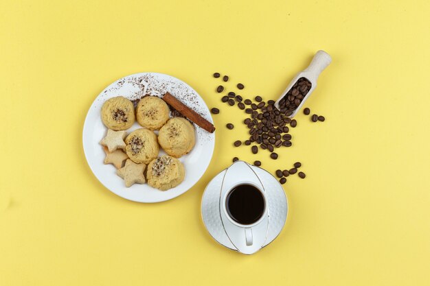 Un poco de café con granos de café, galletas, canela en rama sobre fondo amarillo