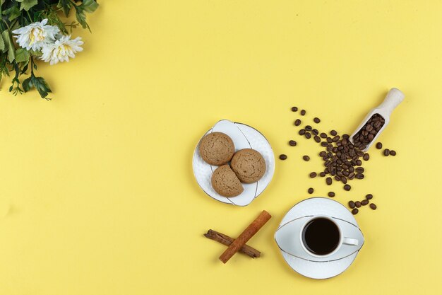 Un poco de café con granos de café, galletas, canela en rama sobre fondo amarillo