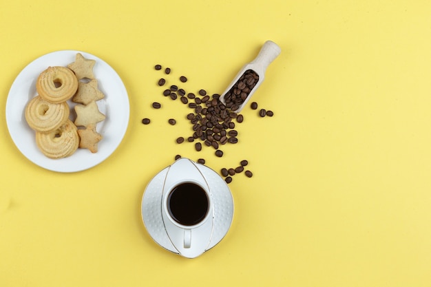 Un poco de café con granos de café y galletas sobre fondo amarillo