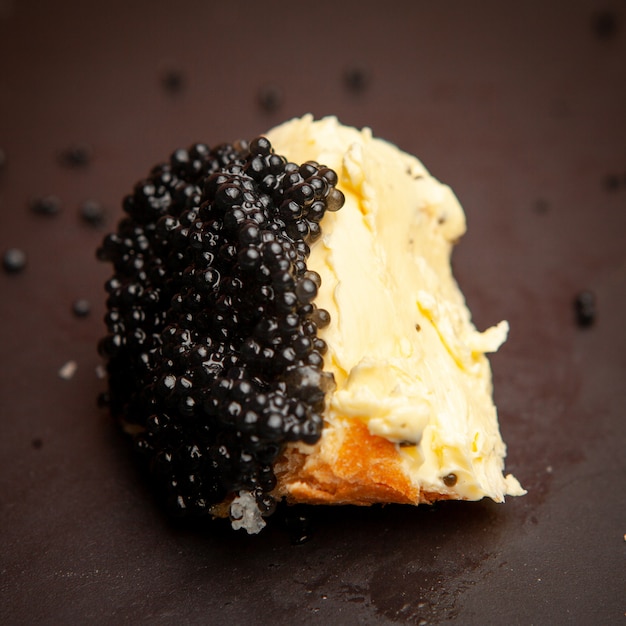 Un poco de caviar negro con mantequilla en el pan en el fondo oscuro, opinión de alto ángulo.