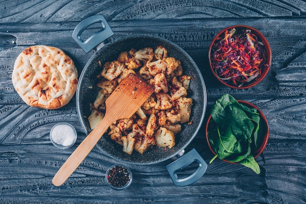 Un poco de coliflor frita con la ensalada vegetal, verde en una olla en el fondo de madera oscuro, visión superior.