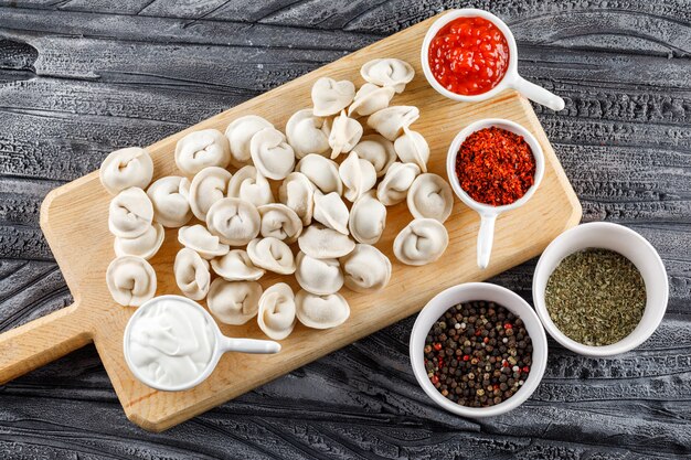 Un poco de masa con salsa, especias en tazones sobre una tabla para cortar sobre la superficie de madera gris, vista desde arriba.