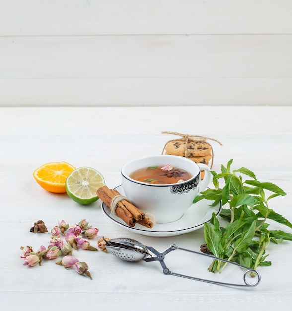 Un poco de té de hierbas con colador de té, hierbas, frutas cítricas y galletas.