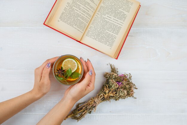 Un poco de té de hierbas con libros y flores sobre superficie blanca