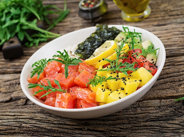 Poke bowl de salmón hawaiano con arroz, aguacate, mango, tomate, semillas de sésamo y algas. Tazón de Buda. Comida dietetica.