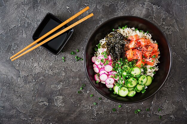 Poke bowl de salmón hawaiano con arroz, rábano, pepino, tomate, semillas de sésamo y algas. Tazón de Buda. Comida dietetica. Vista superior. Endecha plana.