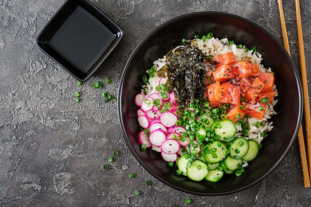 Poke bowl de salmón hawaiano con arroz, rábano, pepino, tomate, semillas de sésamo y algas. Tazón de Buda. Comida dietetica. Vista superior. Endecha plana.