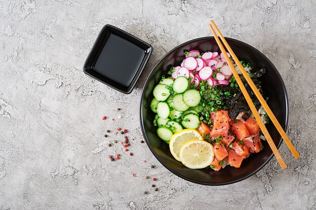 Poke bowl de salmón hawaiano con arroz, rábano, pepino, tomate, semillas de sésamo y algas. Tazón de Buda. Comida dietetica. Vista superior. Endecha plana.