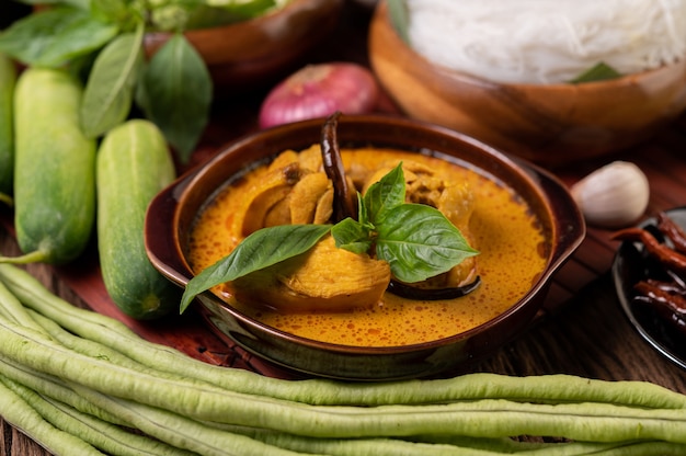 Pollo al curry rojo en un bol con chiles secos, albahaca, pepino y frijoles largos