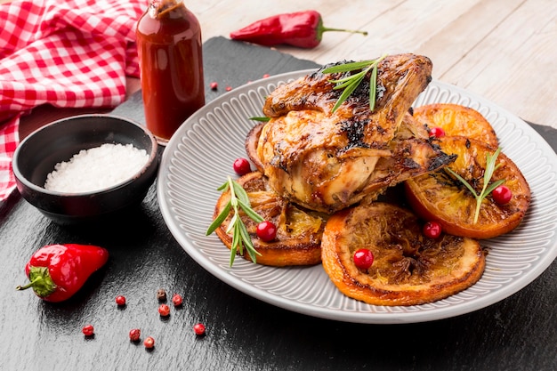 Pollo al horno de alto ángulo y rodajas de naranja en un plato con sal marina