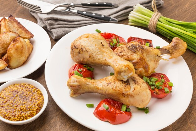 Pollo al horno de alto ángulo y tomates en un plato con gajos y mostaza de Dijon