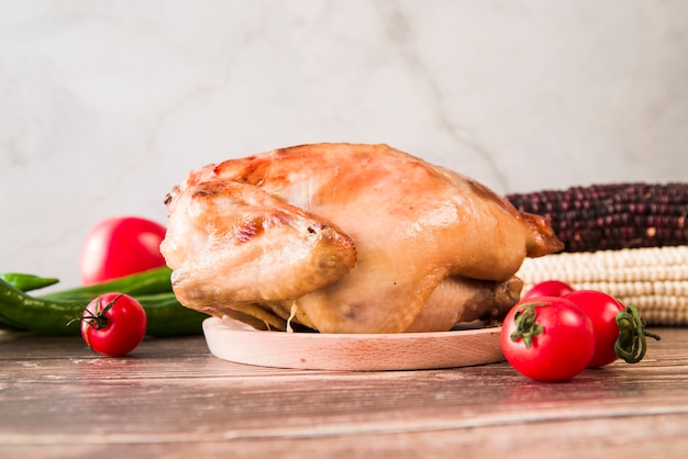 Pollo asado entero con tomates cherry y maíz en mesa de madera