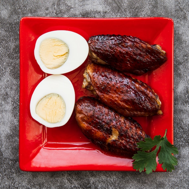 Pollo asado con huevo cocido en plato rojo sobre piso de concreto